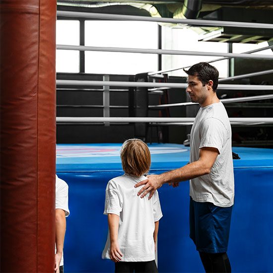 Boxing coach guiding a child inside a boxing ring, placing a hand on the child’s shoulder while giving instructions during training.