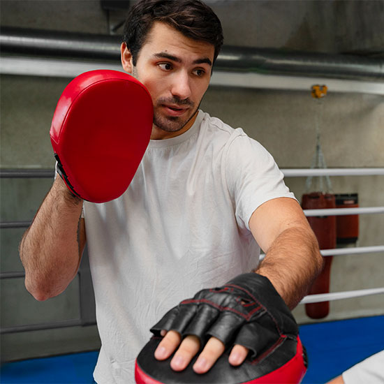 Boxing coach demonstrating pad work with focus mitts inside a boxing gym during a training session.