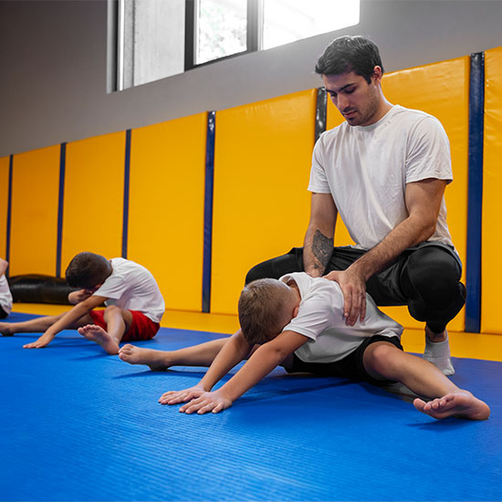 Coach assisting children with stretching exercises on training mats during a kids’ fitness session in a gym.