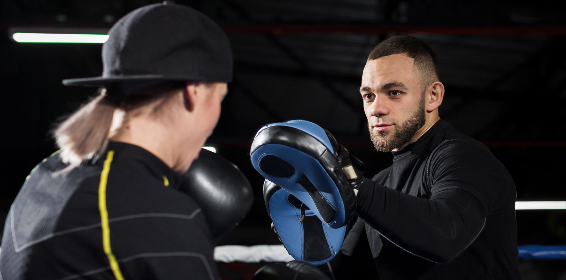 A boxer training with a coach using focus mitts in a boxing gym, practicing striking technique under professional supervision.